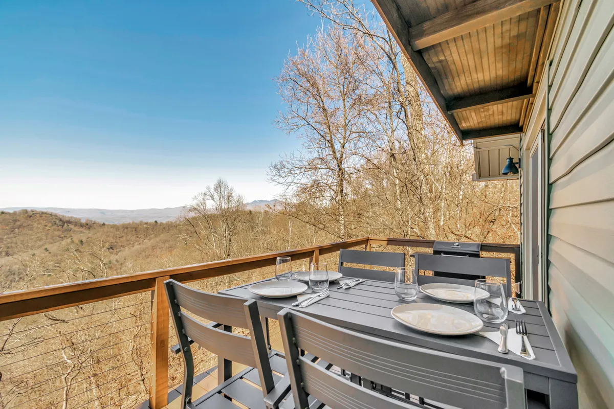 A serene view of an outdoor dining table set against a backdrop of mountain views and tree branches, perfect for morning coffee, outdoor meals, or stargazing under the open sky.