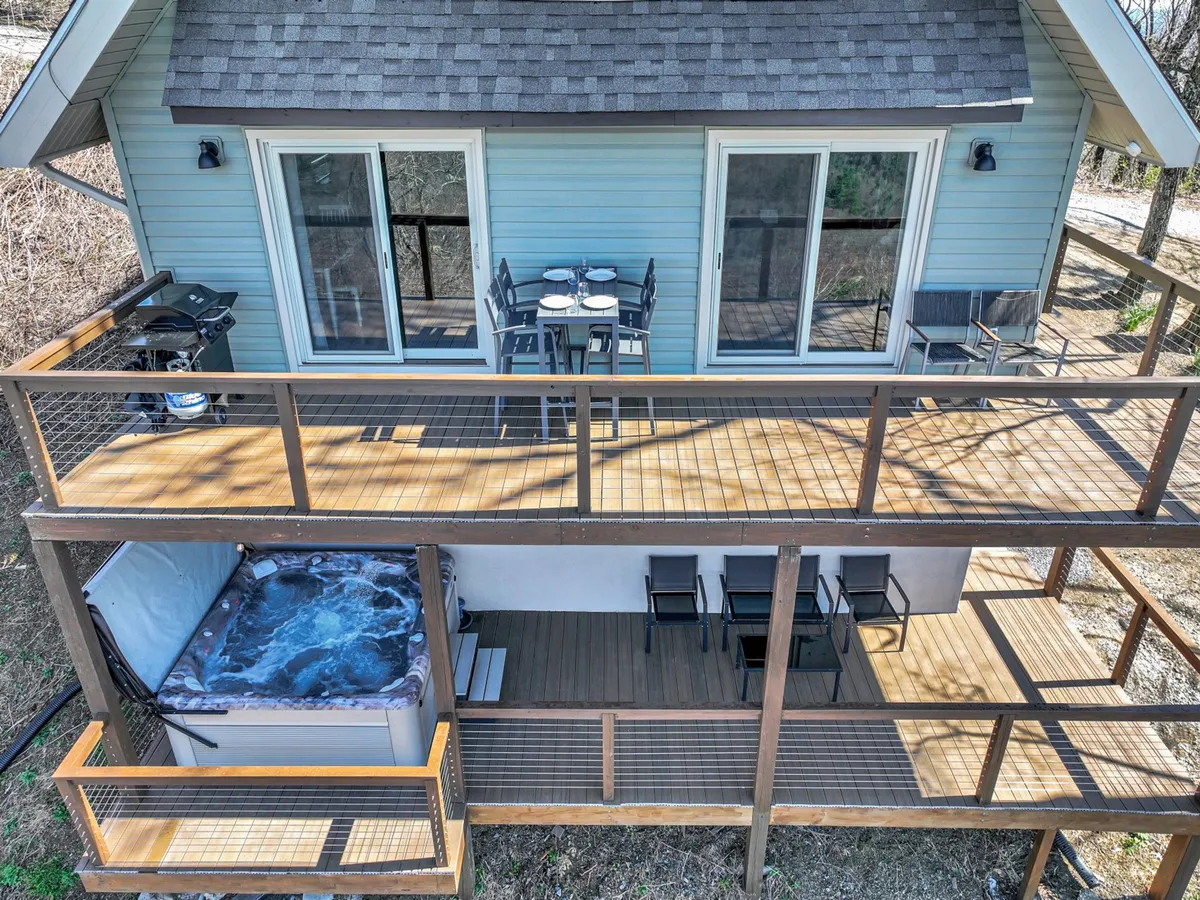 This image captures an inviting exterior deck scene featuring an outdoor dining area, a hot tub, and a grill. The deck looks out onto scenic surroundings, emphasizing both relaxation and communal activity spaces.