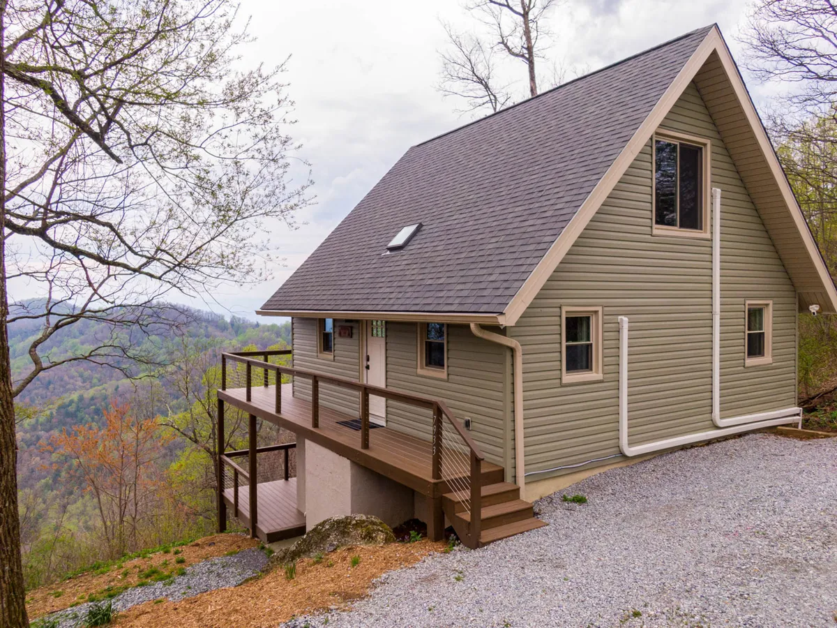 This exterior shot captures the house, its spacious deck, and a breathtaking mountain view stretching into the distance. The deck is inviting, with ample room for family gatherings or relaxing after a day of adventure. The setting sun casts a warm glow, highlighting the connection between the home and the surrounding natural beauty.