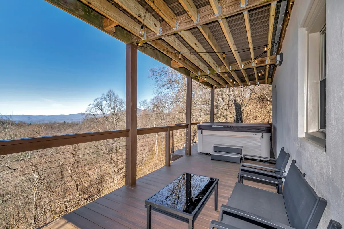 An inviting hot tub sits on a wooden deck, overlooking a peaceful mountain landscape. Outdoor seating nearby suggests a spot to relax after a day of hiking, with scenic views and a tranquil ambiance.