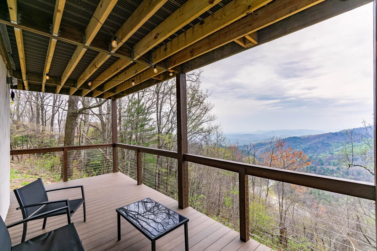 The image features a serene wooden deck furnished with comfortable outdoor seating and a glass table, all set against a stunning mountain view. The inviting atmosphere encourages relaxation, reading, or outdoor work.