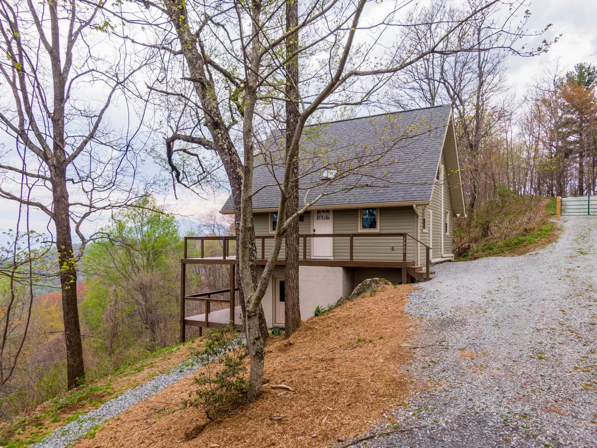 A wider exterior shot of the house, deck area, and surrounding trees, capturing the full structure set into nature. The image hints at the spaciousness and privacy of the property, ideal for groups to spread out and explore.