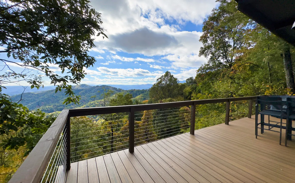 A panoramic view from a wooden deck overlooks an expansive mountain range and a sky scattered with clouds. The peaceful setting hints at opportunities for sunrise coffee or moments of inspiration while gazing into the distance.