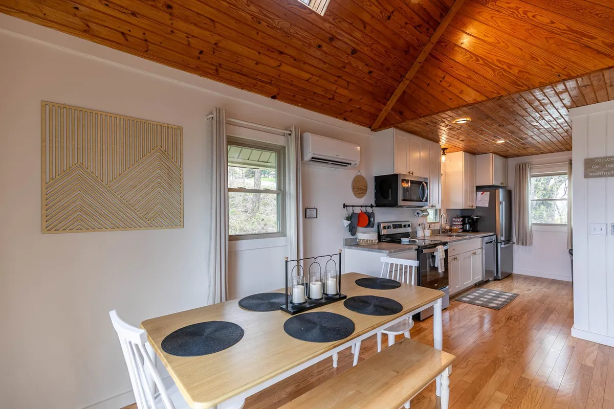 A warmly lit kitchen and dining area with a wooden ceiling, modern appliances, and an adjacent dining table. The kitchen layout is open, and the space exudes a sense of togetherness, inviting guests to cook, dine, and socialize.