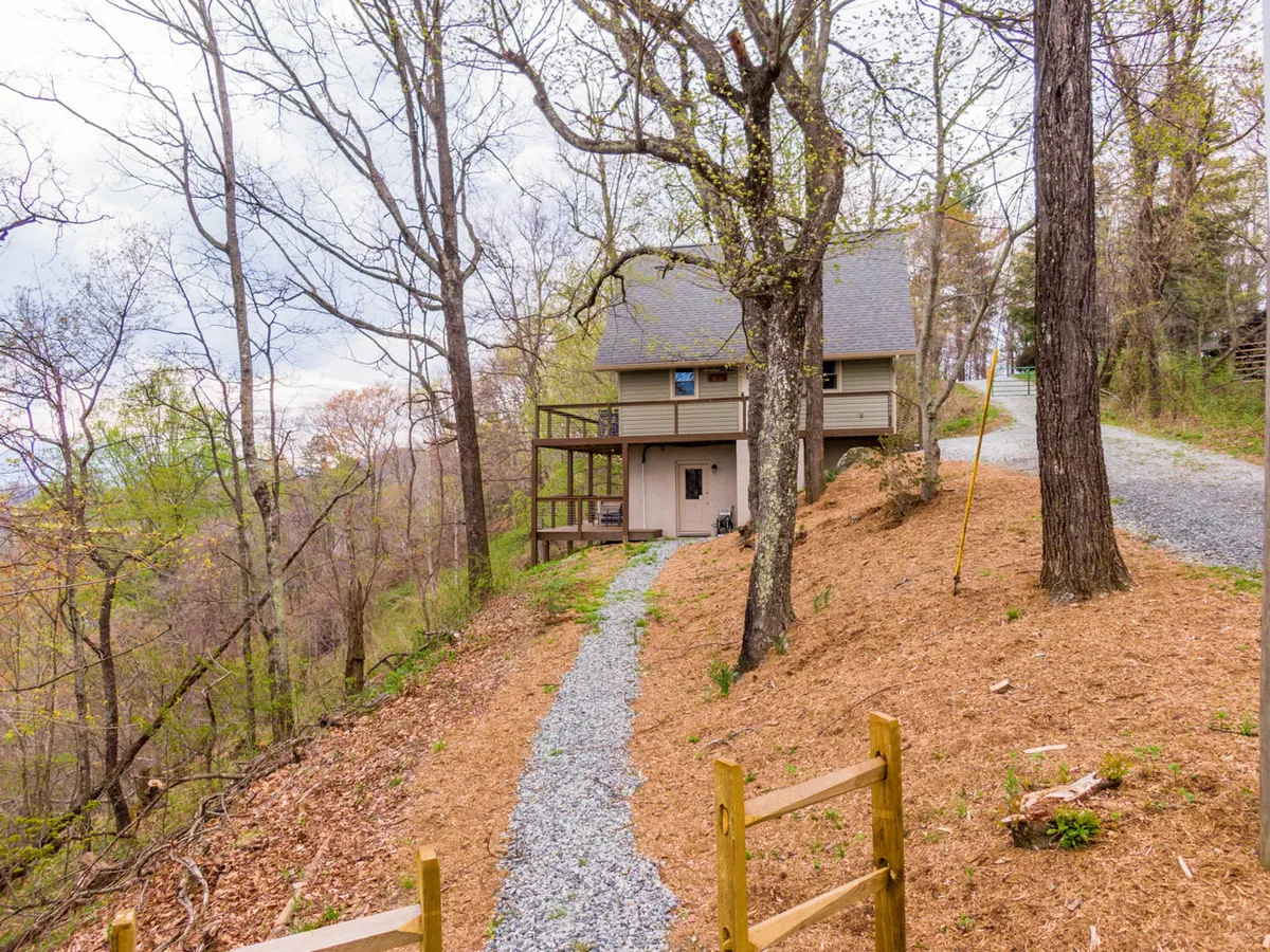 A wide shot of the house nestled among trees with a gravel path leading up to the porch, surrounded by natural beauty. The image evokes the feel of a secluded gateway, inviting families to embark on local hiking trails or nature walks just steps from the front door.
