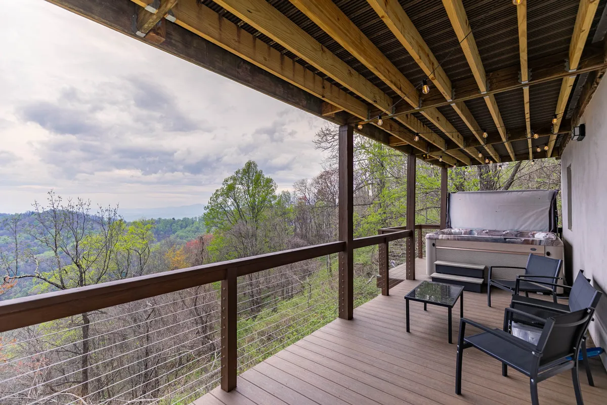 The image features a serene hot tub set on a wooden deck overlooking lush mountains. Comfy seating and open vistas invite guests to relax after an active day, whether soaking at sunset or gathering with family under the stars. The outdoorsy, tranquil vibe is palpable.