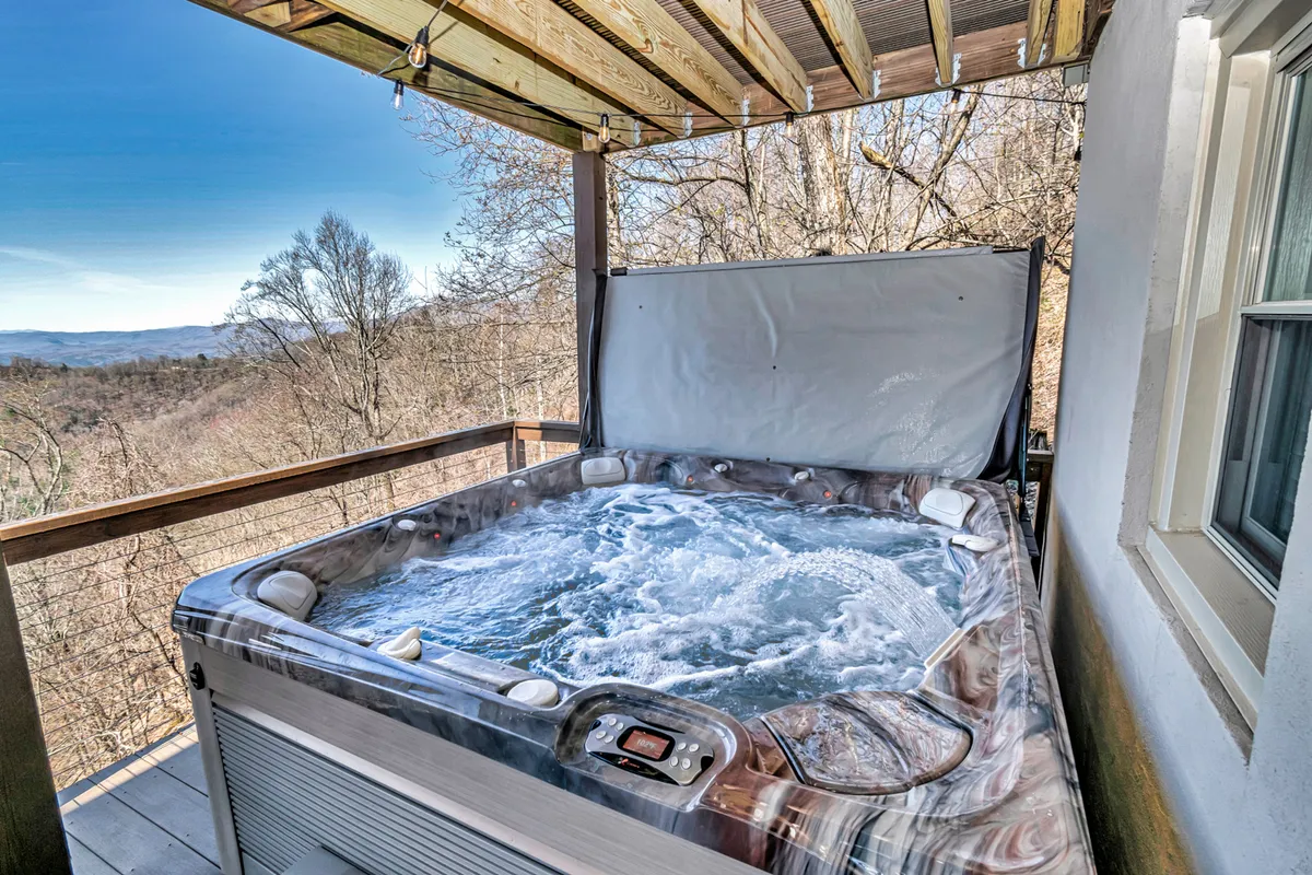 A scenic outdoor deck featuring a bubbling hot tub, wooden decking, and expansive mountain views. The tranquil setting is perfect for unwinding or socializing beneath the open sky.