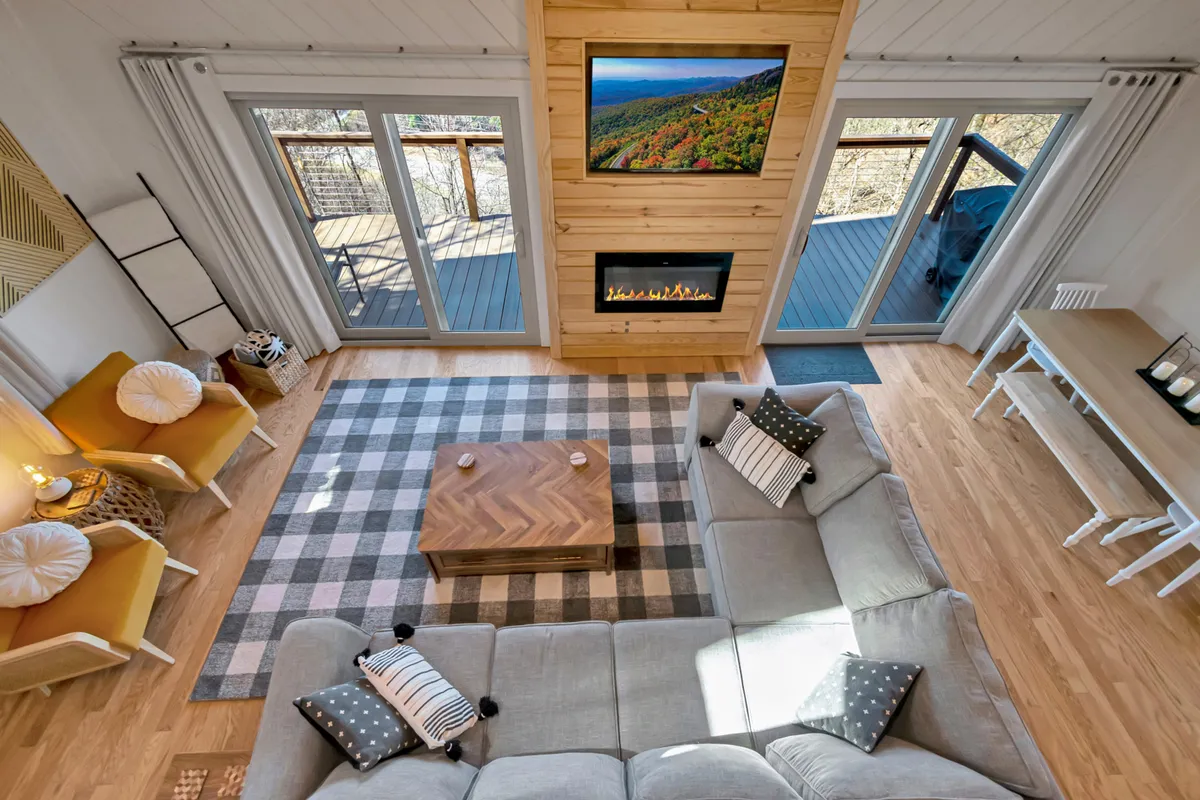 A large sectional sofa faces a fireplace and a TV with a scenic view, complemented by a coffee table and a visible dining area in the background. The room is bright and open, offering spaces for relaxation, entertainment, and shared meals.
